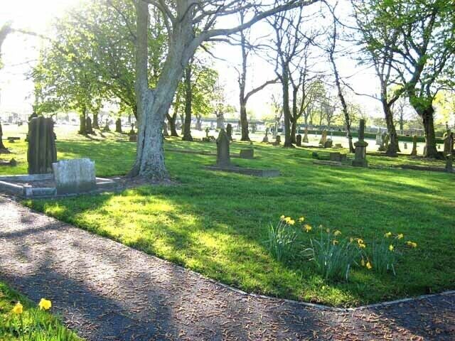 A cemetery with green grass, trees, and tombstones.