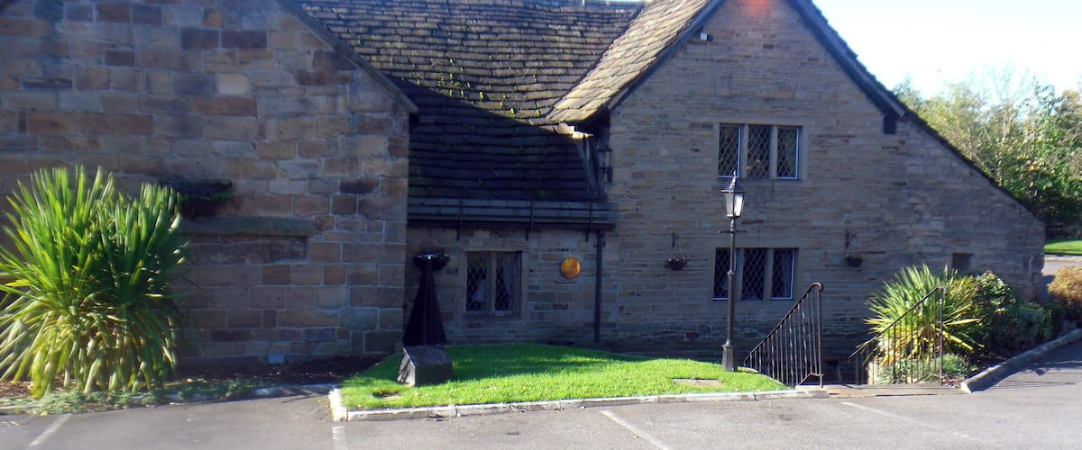 A stone building with a sloped roof, a paved parking area, and some greenery.