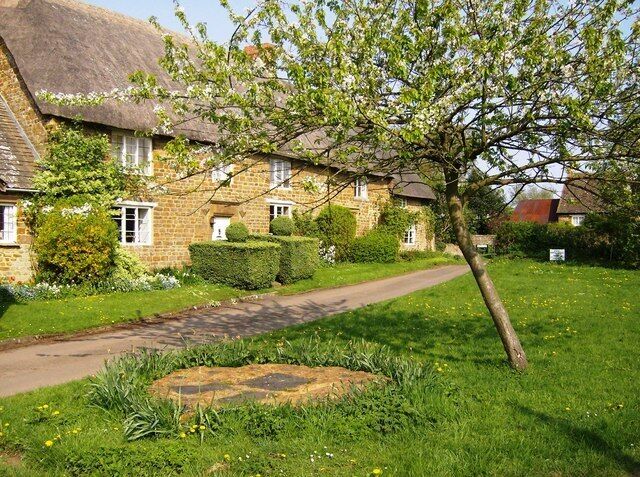 Part of the village green at Epwell, Oxfordshire. On the left is Village House, with Charlie's Cottage beyond. Both are thatched 17th-century stone cottages. The stone area with grey slates in the foreground is a sundial. See 449049