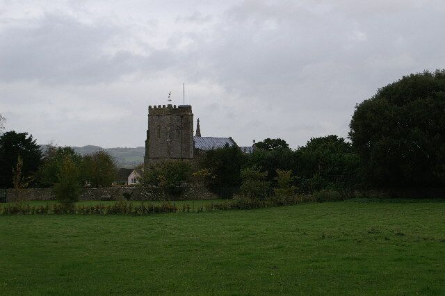 A church with a tall tower, surrounded by a grassy field and trees.