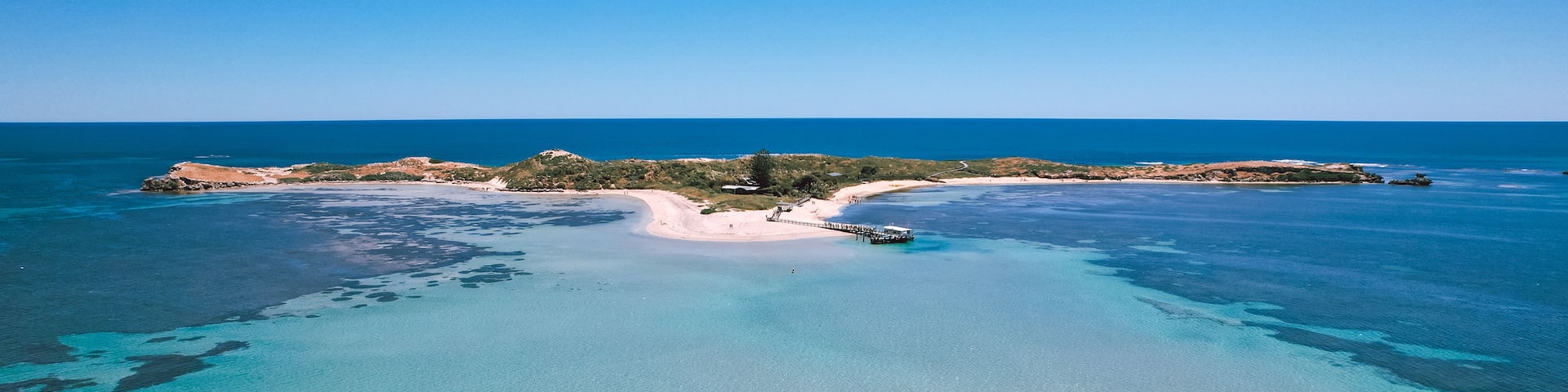 A coastal landscape with clear turquoise waters, a sandy beach, and a small island with vegetation.