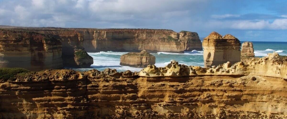 A coastal landscape with layered rock formations and a clear sky.