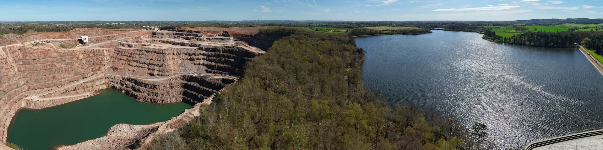 A large open-pit mine adjacent to a river with a clear sky.