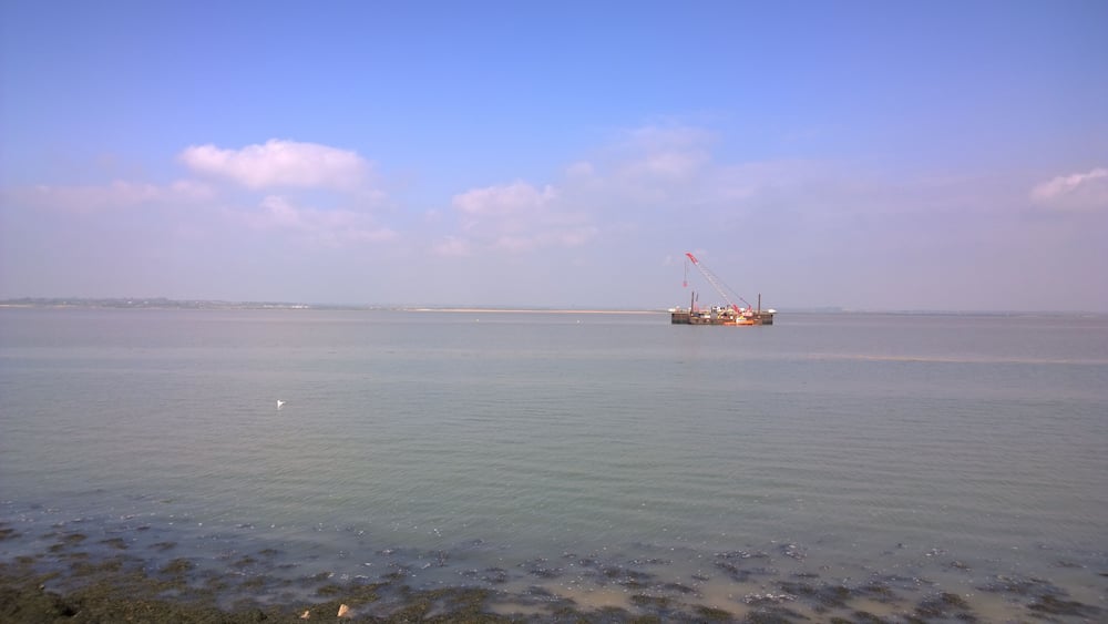 Une mer calme avec une plateforme pétrolière visible au loin.