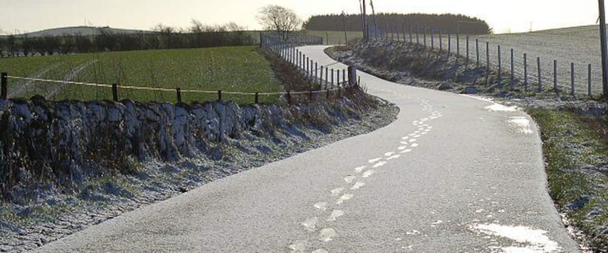 A rural road curving through a field with a stone wall on one side and a fence on the other.