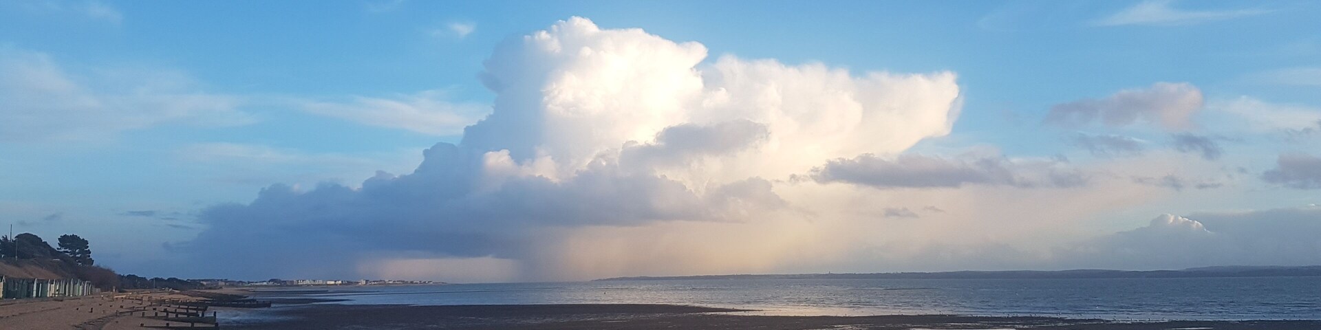 Una playa de guijarros, una gran nube y una costa distante.