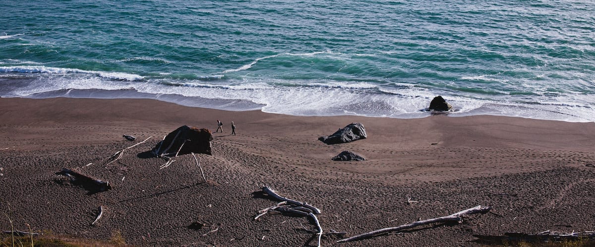 A rocky coastline with waves crashing onto the shore and a large rock formation in the distance.