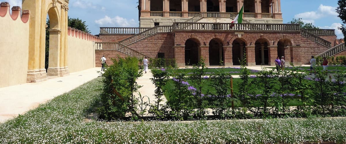 A historic building with a central courtyard, surrounded by a garden with white and purple flowers.
