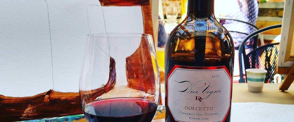 A bottle of Due Vigne wine and a glass of red wine on a table with a painting in the background.