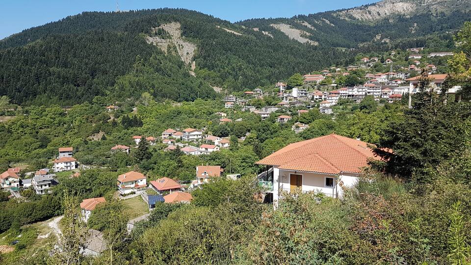 A hillside village with red-tiled roofs, surrounded by dense forest and mountains.