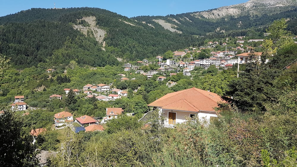 Ένα χωριό χτισμένο σε πλαγιά λόφου, με σπίτια που είναι τοποθετημένα σε διαδοχικά επίπεδα και περιβάλλεται από πυκνό δάσος.