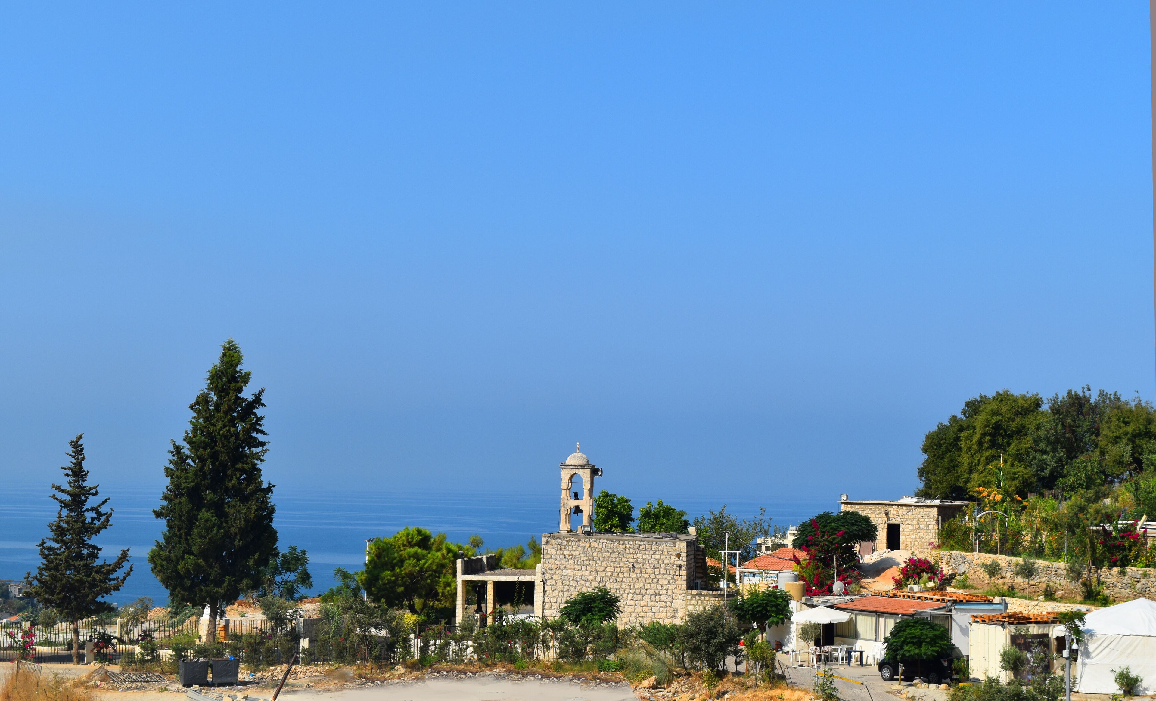 A coastal village with stone buildings, a church tower, and a clear view of the sea.