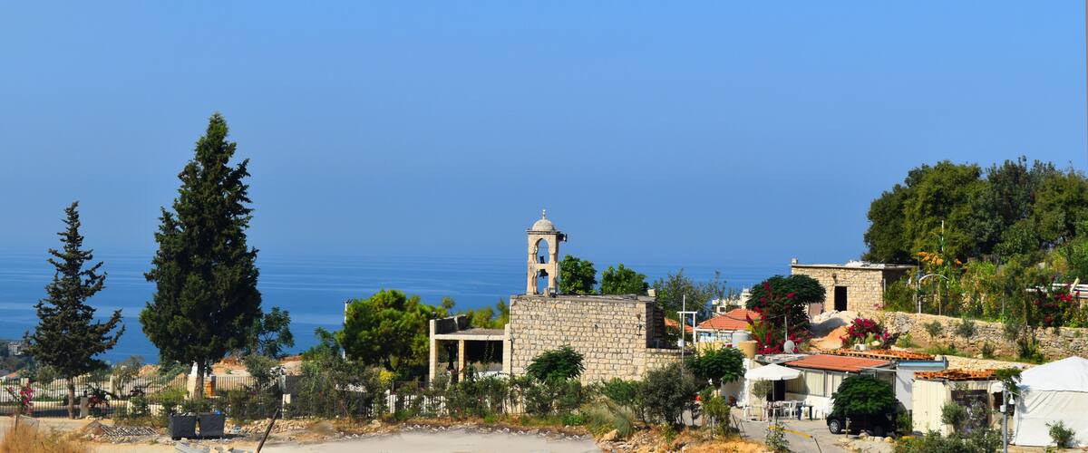 A coastal village with stone buildings, a church tower, and a clear view of the sea.
