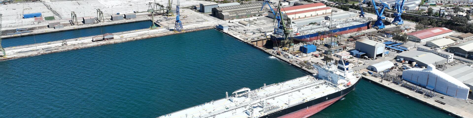 A large cargo ship docked at a port with cranes and industrial buildings in the background.