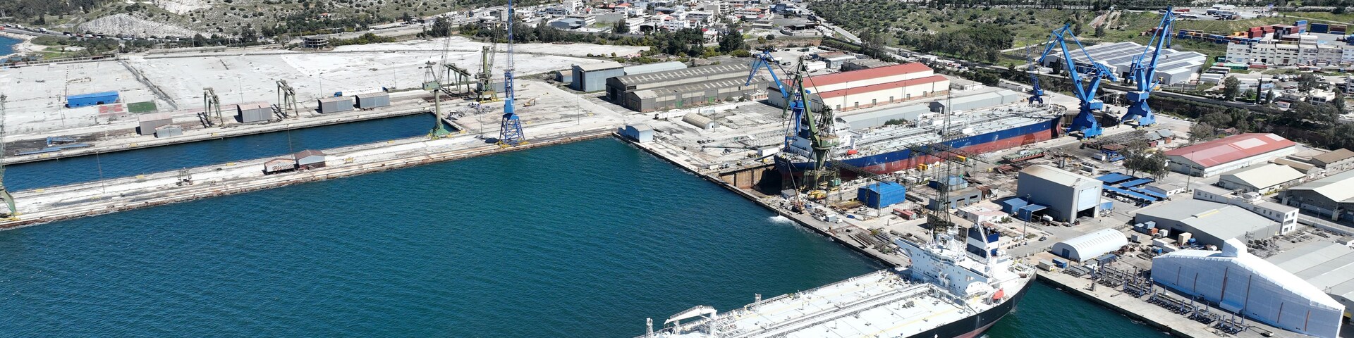 Un gran buque de carga atracado en un puerto con grúas y edificios industriales al fondo.