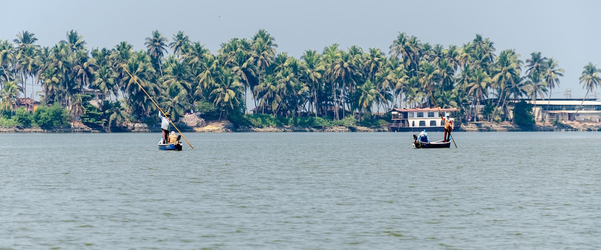 Two boats on calm water with a backdrop of palm trees and a building.