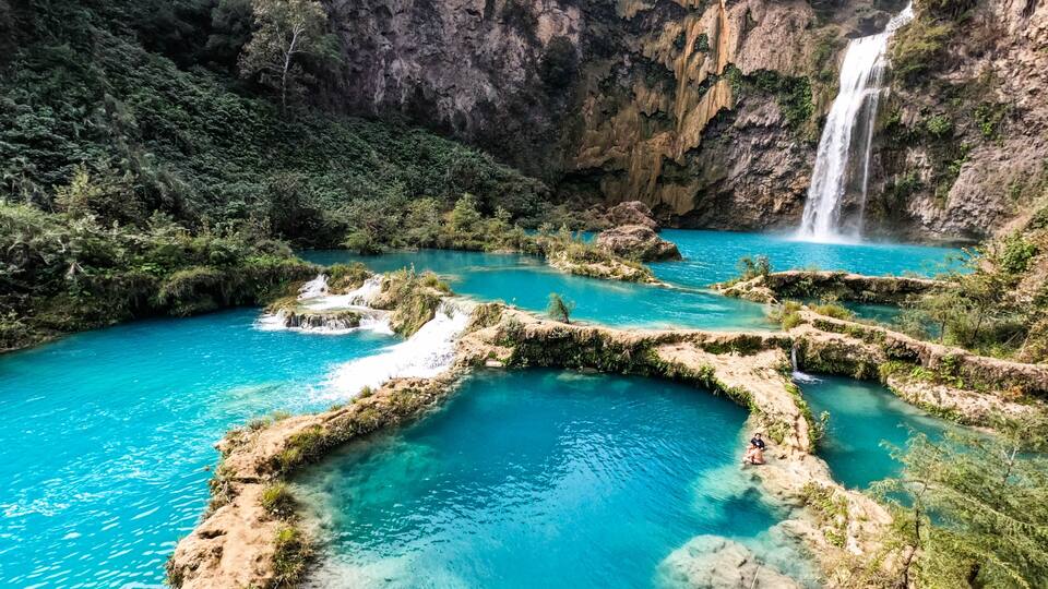 A turquoise river with rocky formations and a waterfall.
