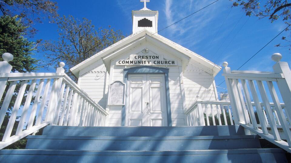 A white church with a cross on top, named Creston Community Church, with a porch and steps leading up to the entrance.