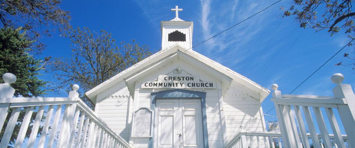 A white church with a cross on top, named Creston Community Church, with a porch and steps leading up to the entrance.