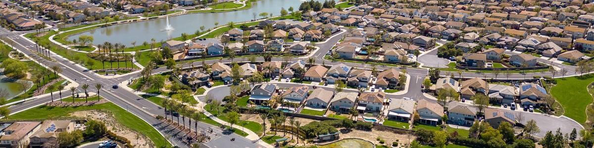 Drone photos over The Lakes community in Discovery Bay, California with houses, houses with solar, a lake with fountains, roadways and a beautiful blue sky with room for text