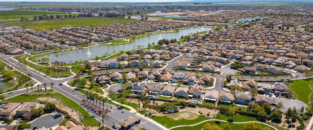Drone photos over The Lakes community in Discovery Bay, California with houses, houses with solar, a lake with fountains, roadways and a beautiful blue sky with room for text