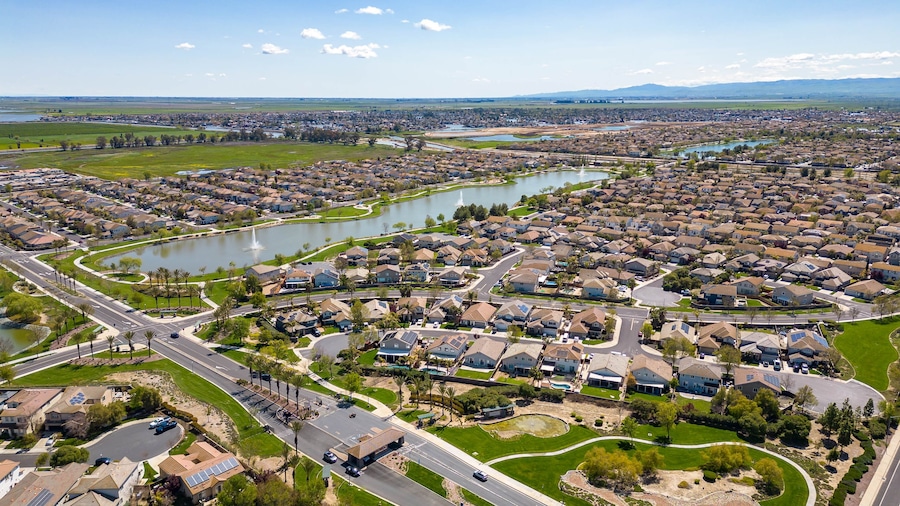 Drone photos over The Lakes community in Discovery Bay, California with houses, houses with solar, a lake with fountains, roadways and a beautiful blue sky with room for text