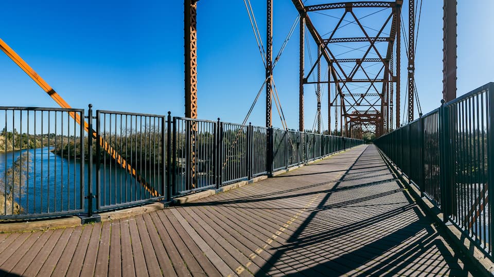 A wooden pedestrian bridge with metal railings, overlooking a body of water.