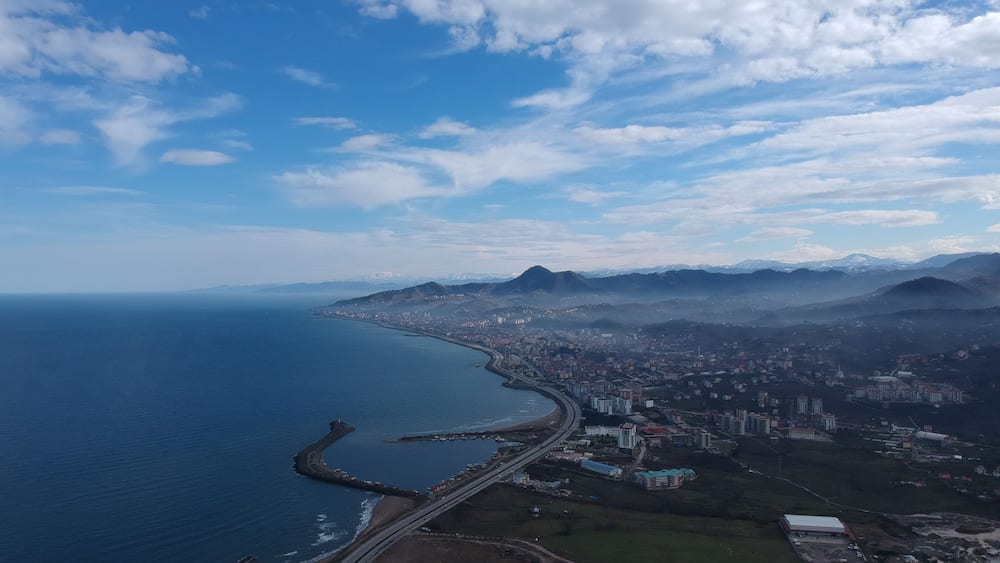 A coastal city with a prominent bridge, mountains in the background, and a clear sky.