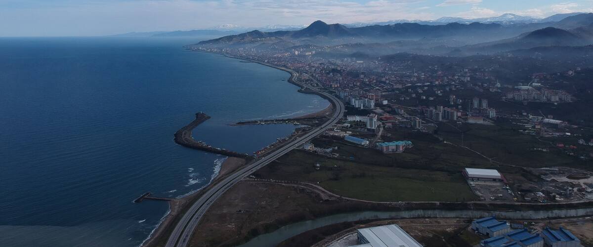 A coastal city with a prominent bridge, mountains in the background, and a clear sky.