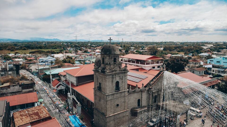 A historic church with a bell tower, surrounded by residential buildings and a mountainous landscape in the background.
