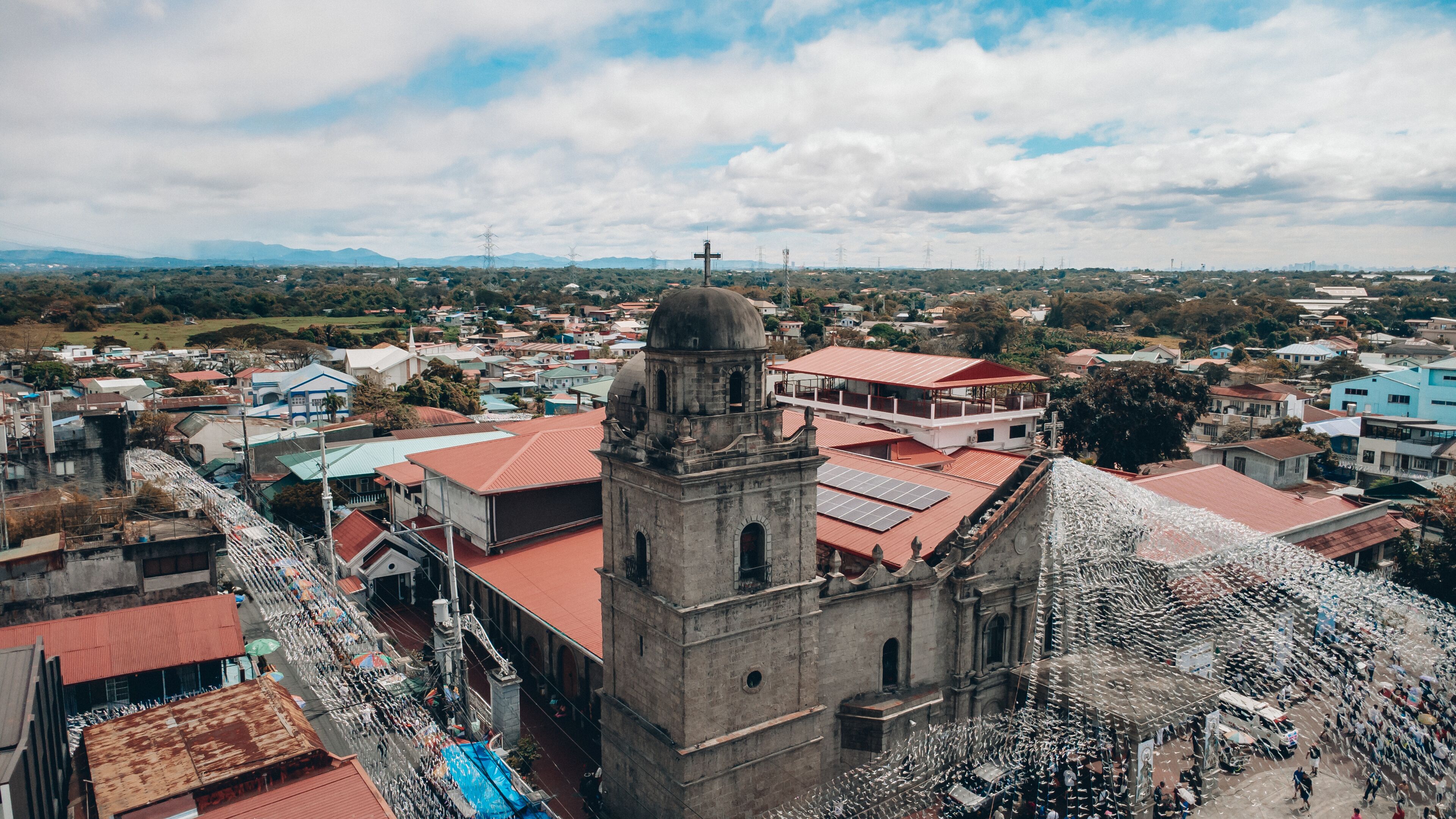 A historic church with a bell tower, surrounded by residential buildings and a mountainous landscape in the background.