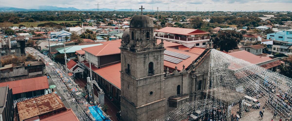 A historic church with a bell tower, surrounded by residential buildings and a mountainous landscape in the background.