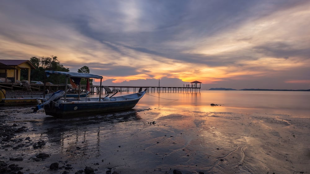 A boat docked at a pier with a sunset in the background.
