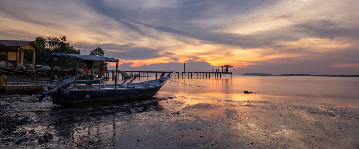 A boat docked at a pier with a sunset in the background.