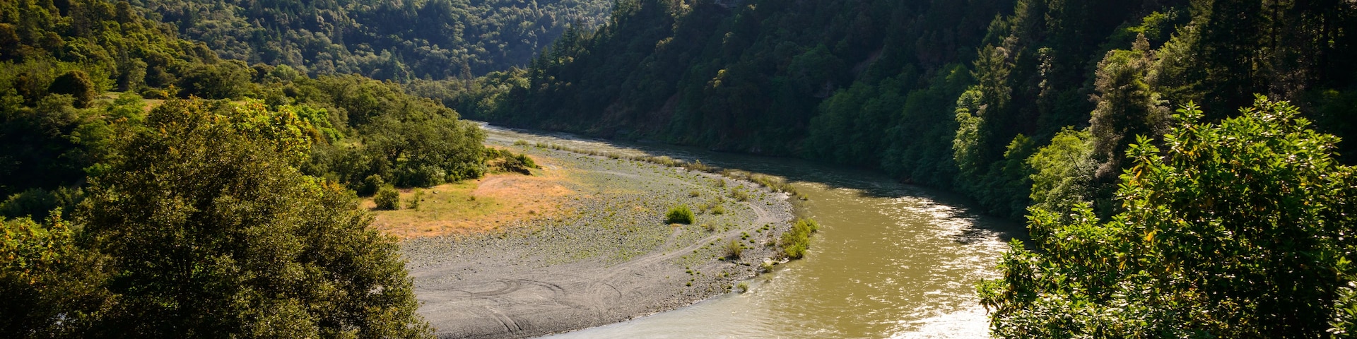Une rivière serpente à travers une vallée boisée, avec des collines en arrière-plan.