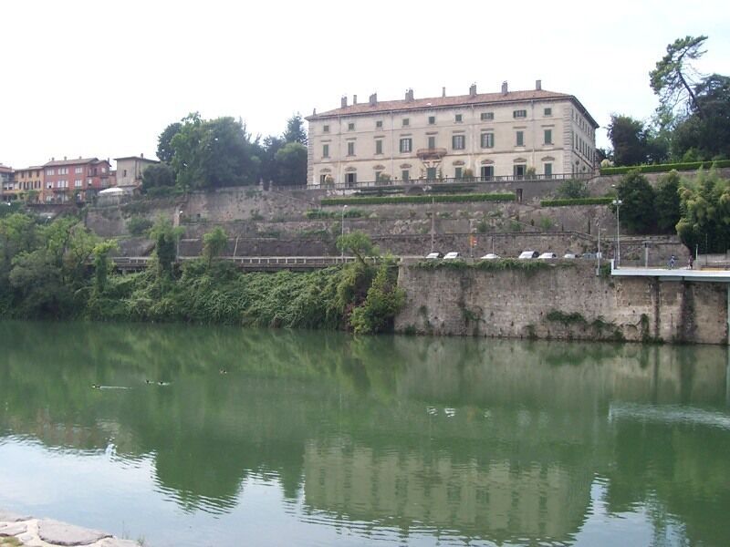 A calm river with a stone wall and a large building in the background.