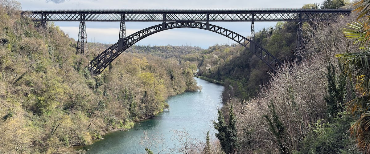 Un puente de acero que cruza un río, rodeado de vegetación densa y colinas.