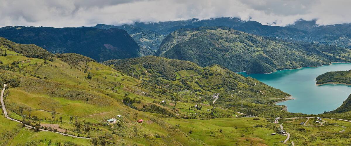 A mountainous landscape with a turquoise lake surrounded by lush green hills and a winding road.