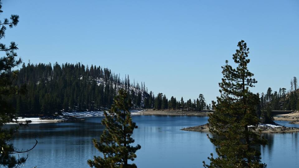 A calm lake surrounded by dense forest and snow patches.
