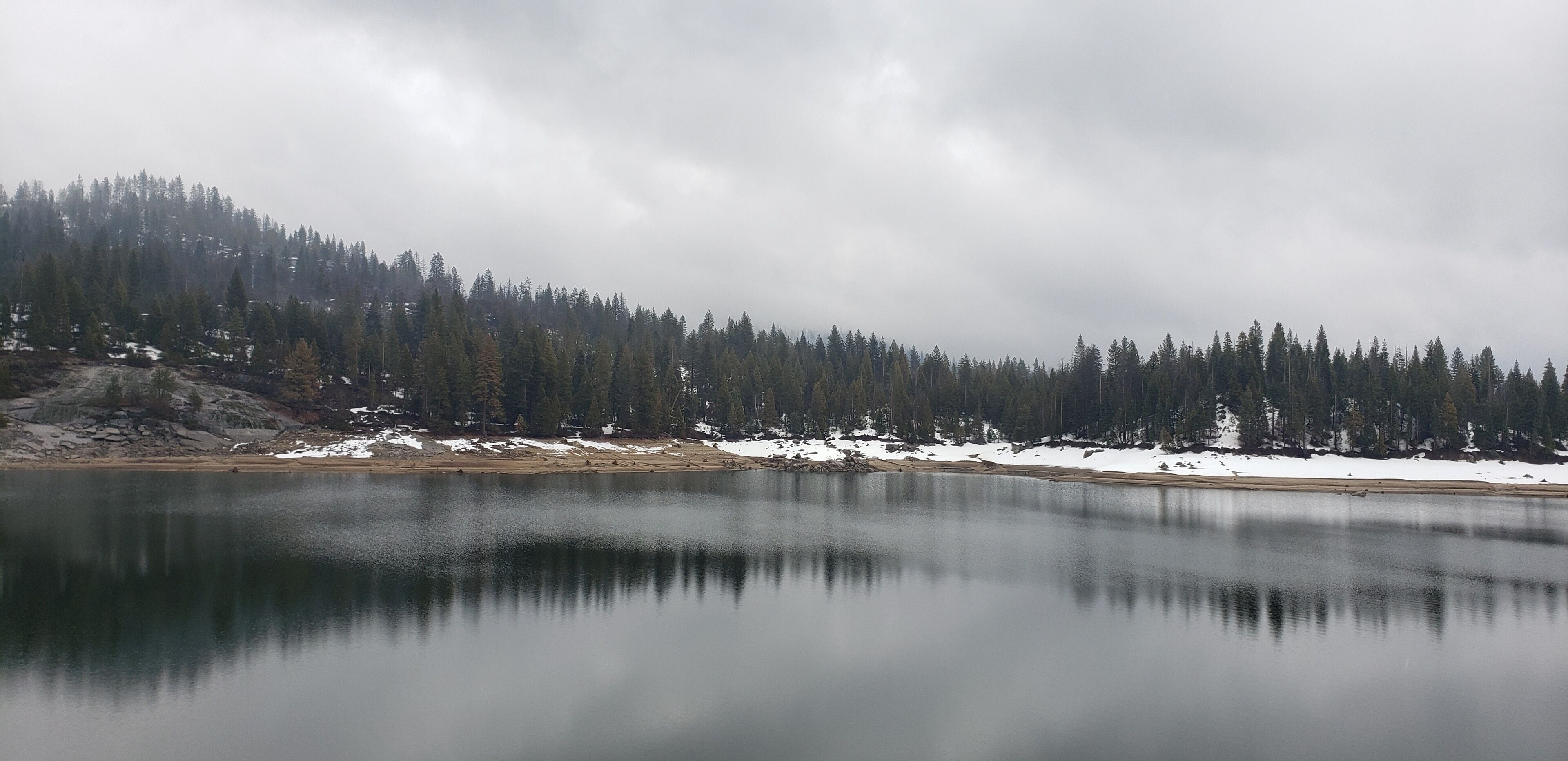 A calm lake surrounded by snow-covered ground and dense forest.