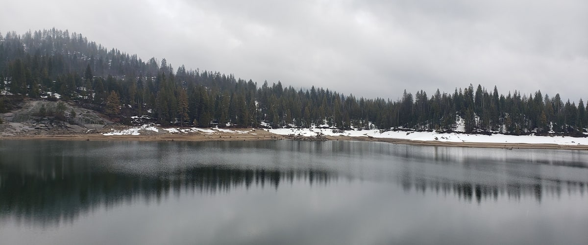 A calm lake surrounded by snow-covered ground and dense forest.