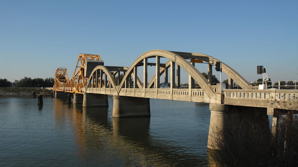A steel bridge over a calm river with concrete supports.
