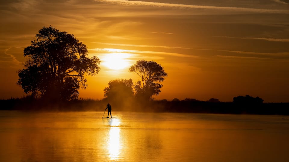 A sunset over a calm lake with a person paddleboarding.