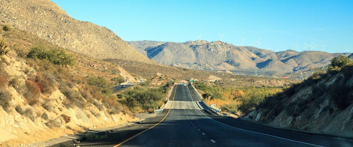 A highway with wind turbines in the distance, surrounded by mountainous terrain.