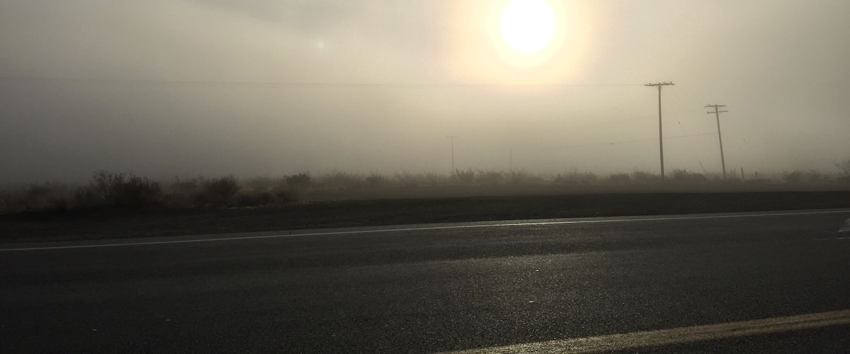 A road with a bright sun in the distance, surrounded by fog.