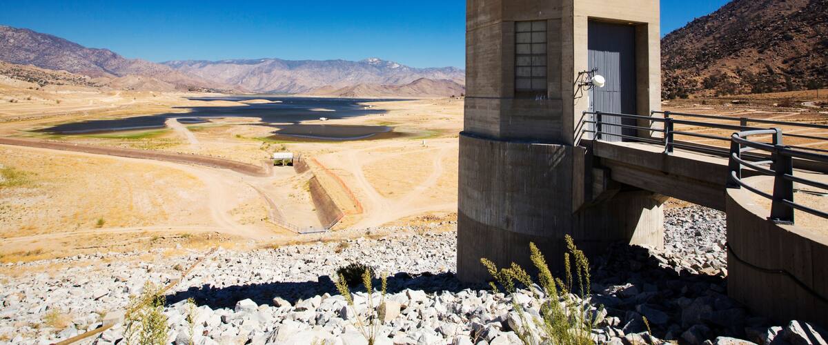 A concrete structure labeled 'ISABELLA DAM' with a bridge, a dry lakebed, and mountains in the background.