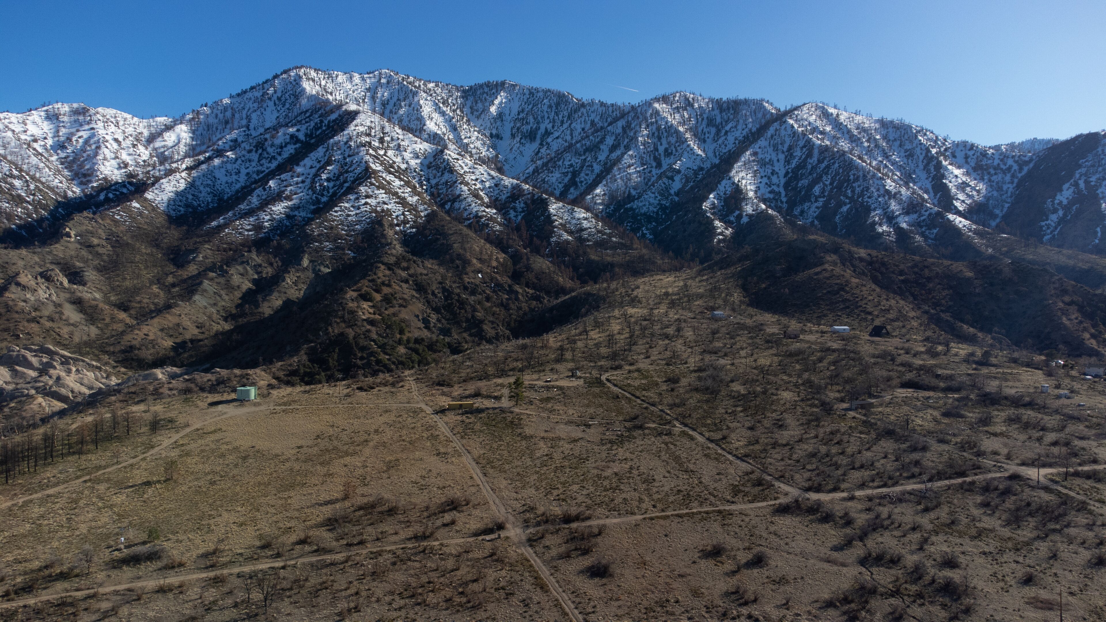 A mountainous landscape with snow-capped peaks and a dry valley below.