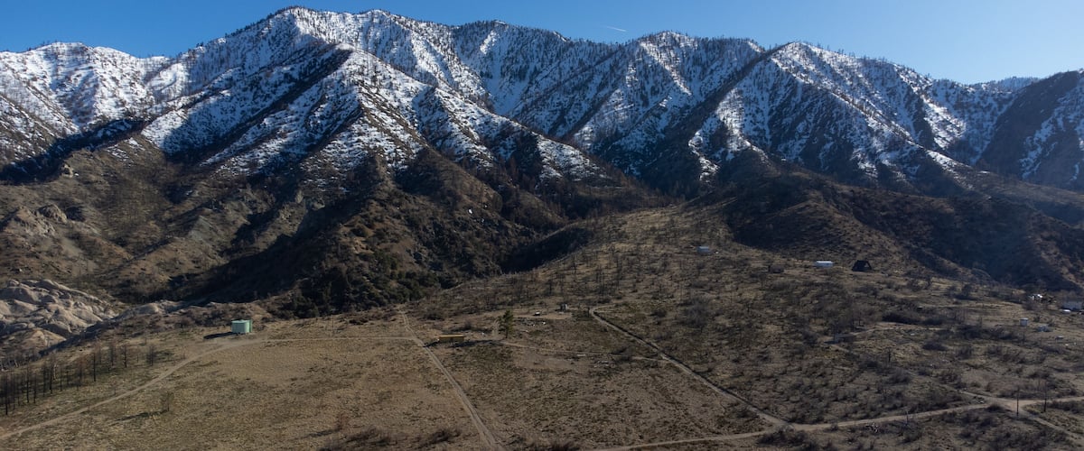 A mountainous landscape with snow-capped peaks and a dry valley below.
