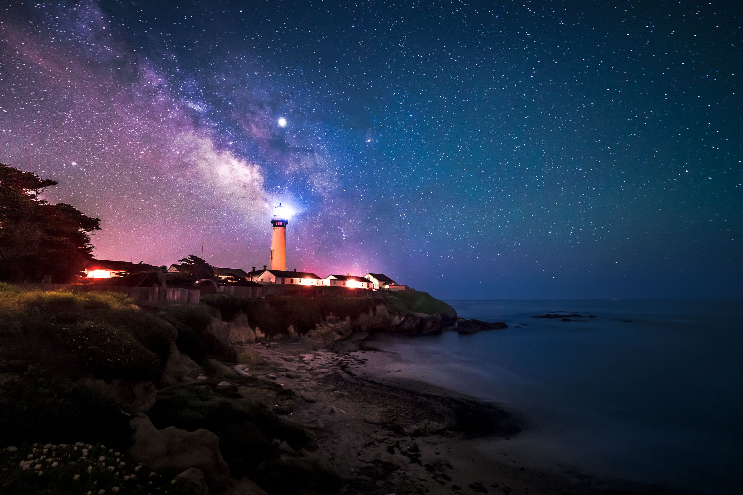 Un faro de noche bajo un cielo estrellado y la Vía Láctea.