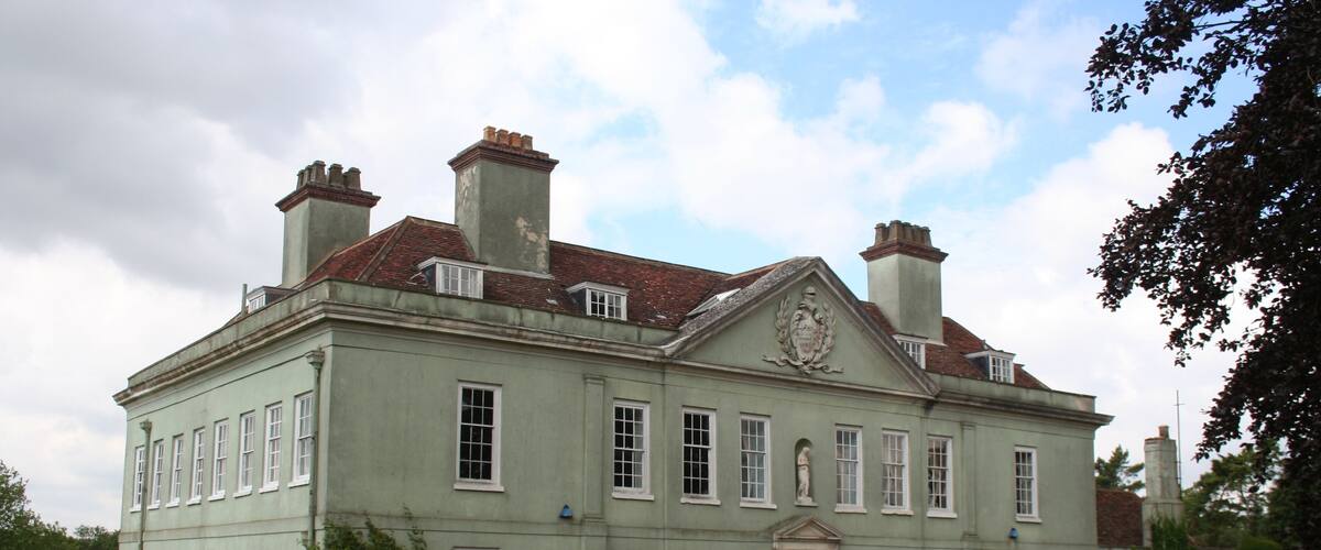 A large, historic building with a symmetrical facade, multiple chimneys, and a central entrance with a decorative pediment.